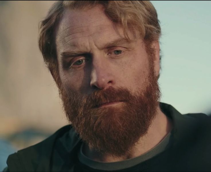 a close up of a man with a beard wearing a black shirt and looking at the camera