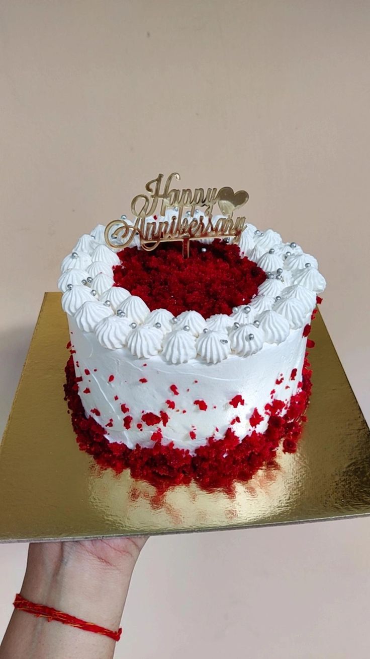 a hand holding a cake with red and white frosting