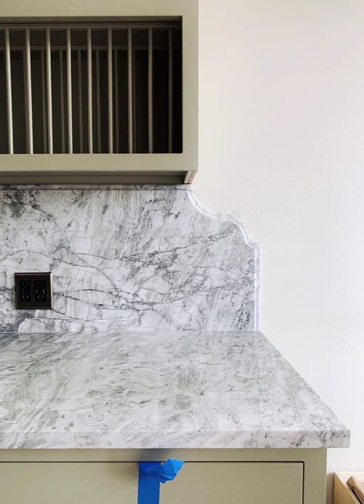 a white marble counter top in a kitchen with blue tape on the bottom and an oven vent above it