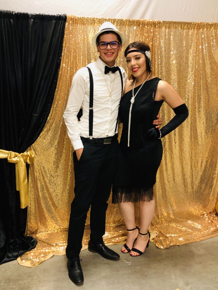 a man and woman standing next to each other in front of a gold curtain backdrop