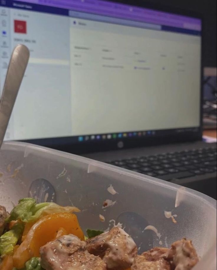 a plastic container filled with meat and veggies next to a laptop computer on a desk