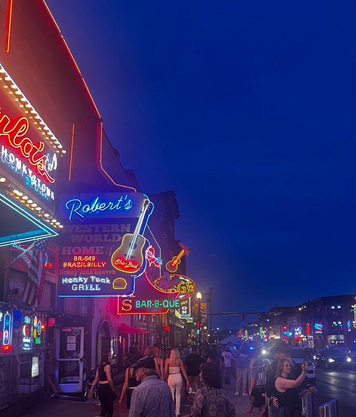 people walking down the street at night with neon signs and guitars on the buildings in the background