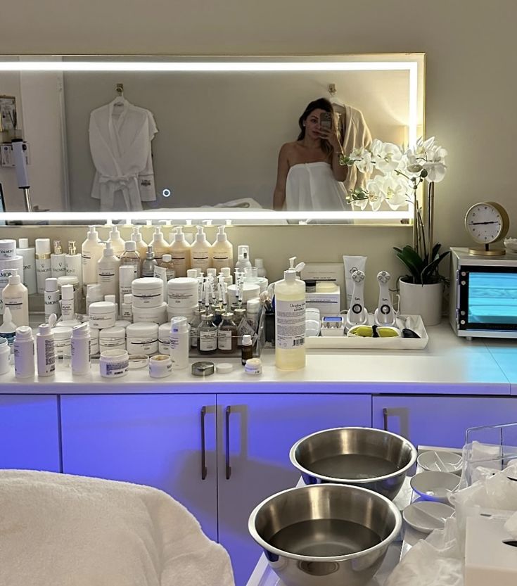 a woman is looking in the mirror at her personal care products and bathrobe