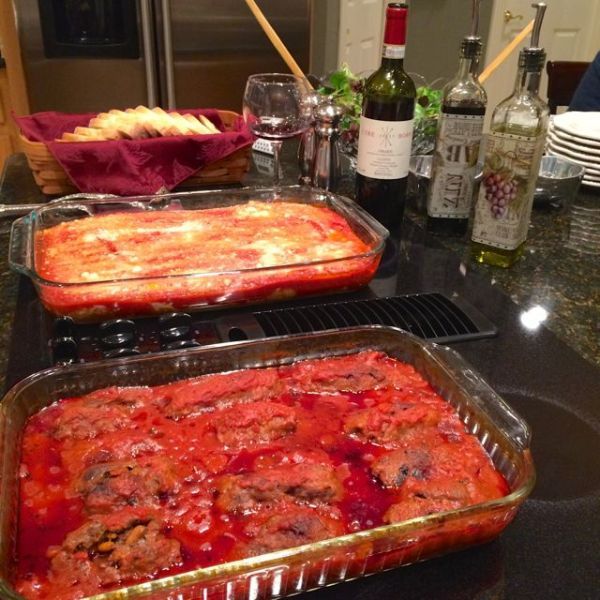 two pans filled with food sitting on top of a counter next to bottles of wine