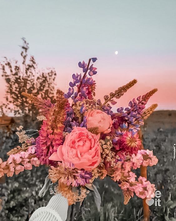 a vase filled with lots of pink flowers on top of a wooden table next to a field