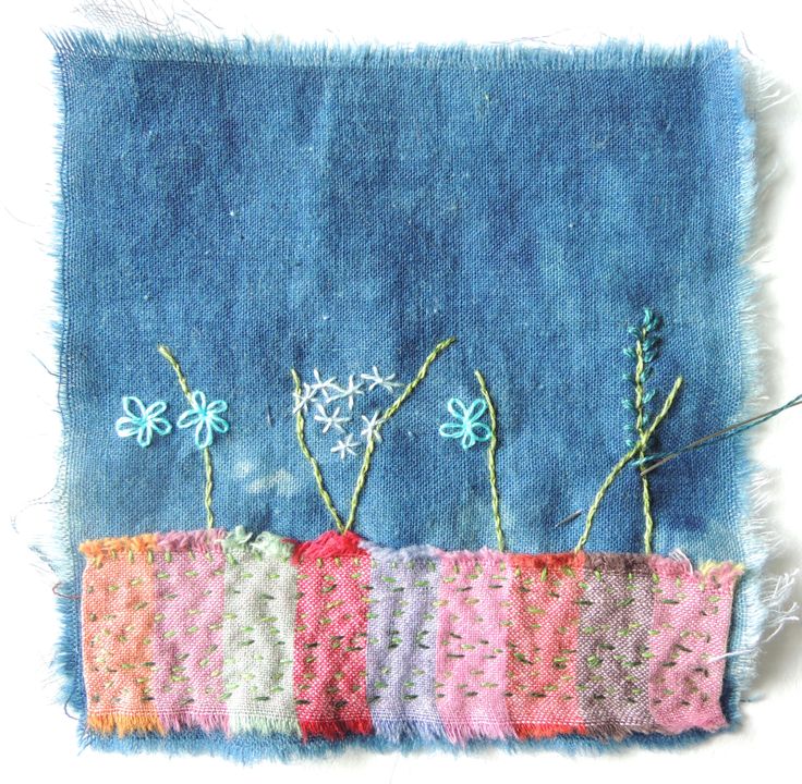 an embroidered piece of cloth with flowers in it on a white surface, next to a blue background