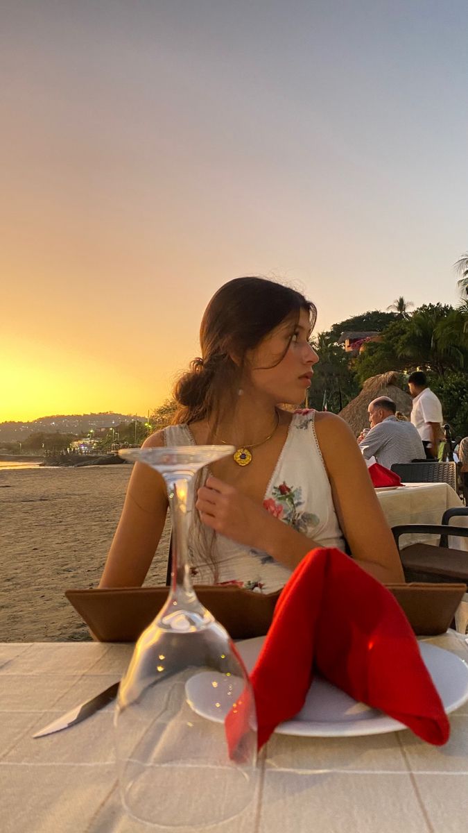 a woman sitting at a table in front of an empty wine glass on the beach