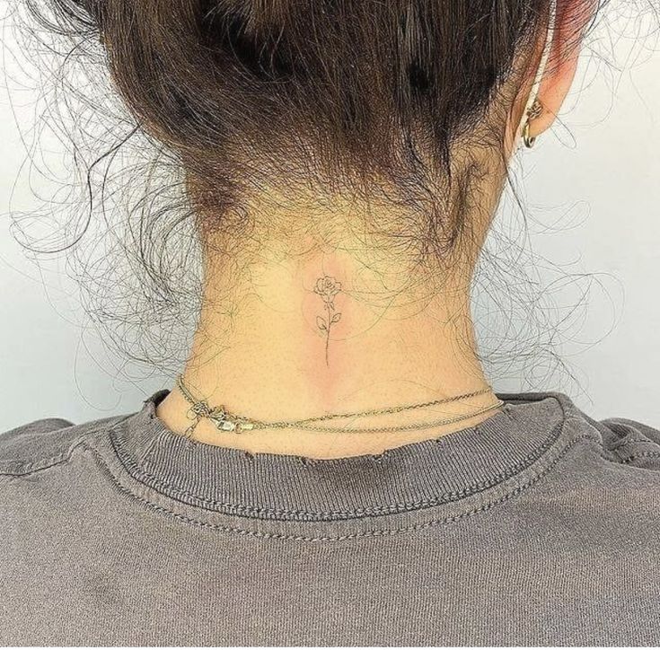 the back of a woman's neck with a small flower tattoo on her left side