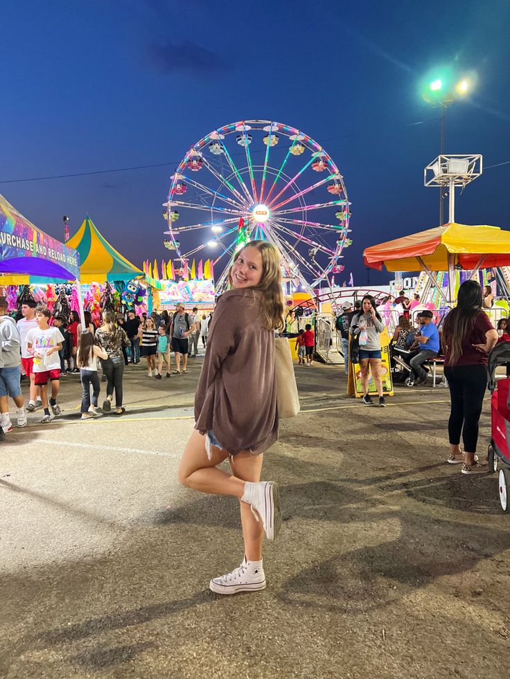 a woman standing in front of a carnival with ferris wheel in the background at night