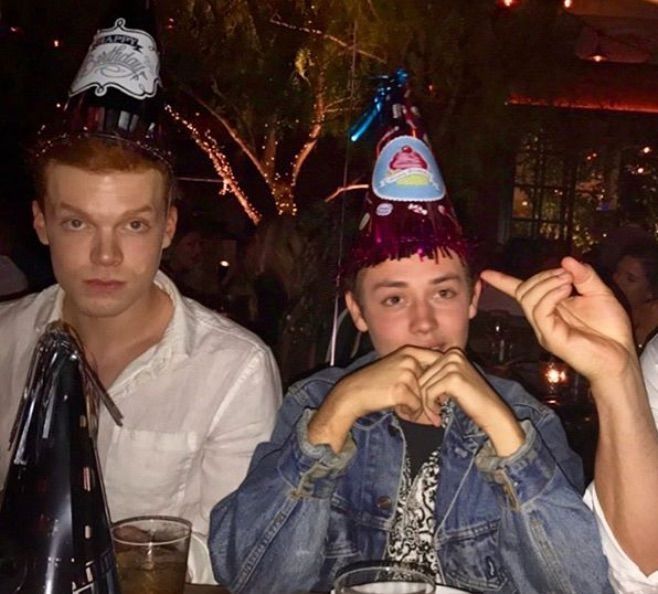 three men sitting at a table with drinks and hats on their heads, one man is pointing to the side