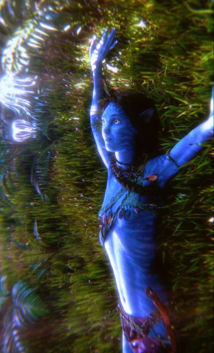 a woman with blue paint on her body and hands in the air, surrounded by plants