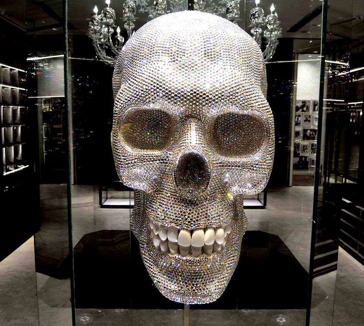 a crystal skull in a glass case with chandeliers on the wall behind it