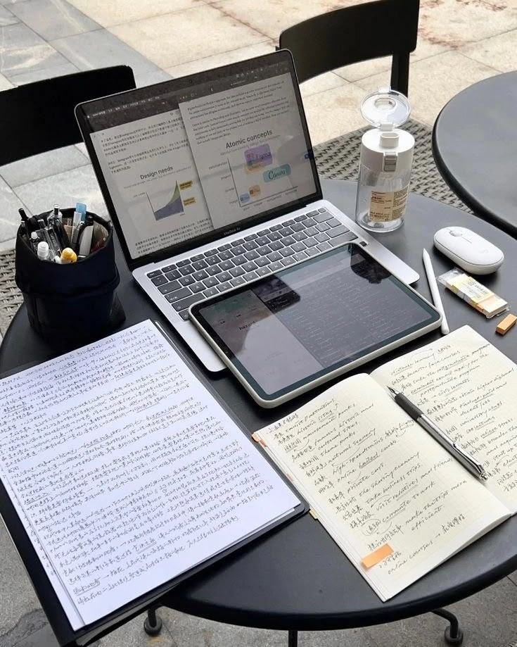 an open laptop computer sitting on top of a black table next to two notebooks