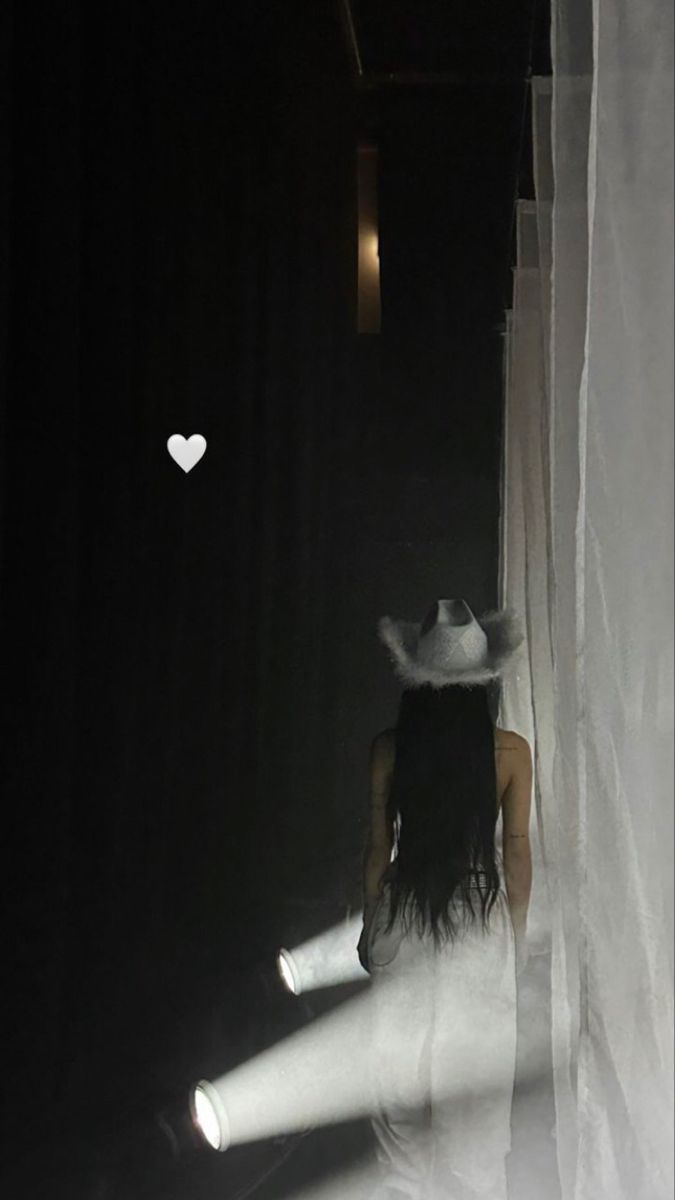 a woman walking down a dark hallway next to a white curtain with a heart on it