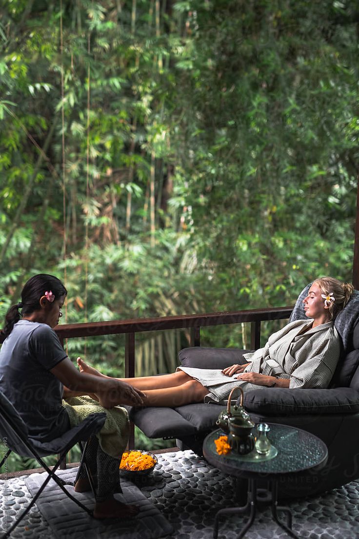 a woman sitting in a chair on top of a patio next to a man laying down