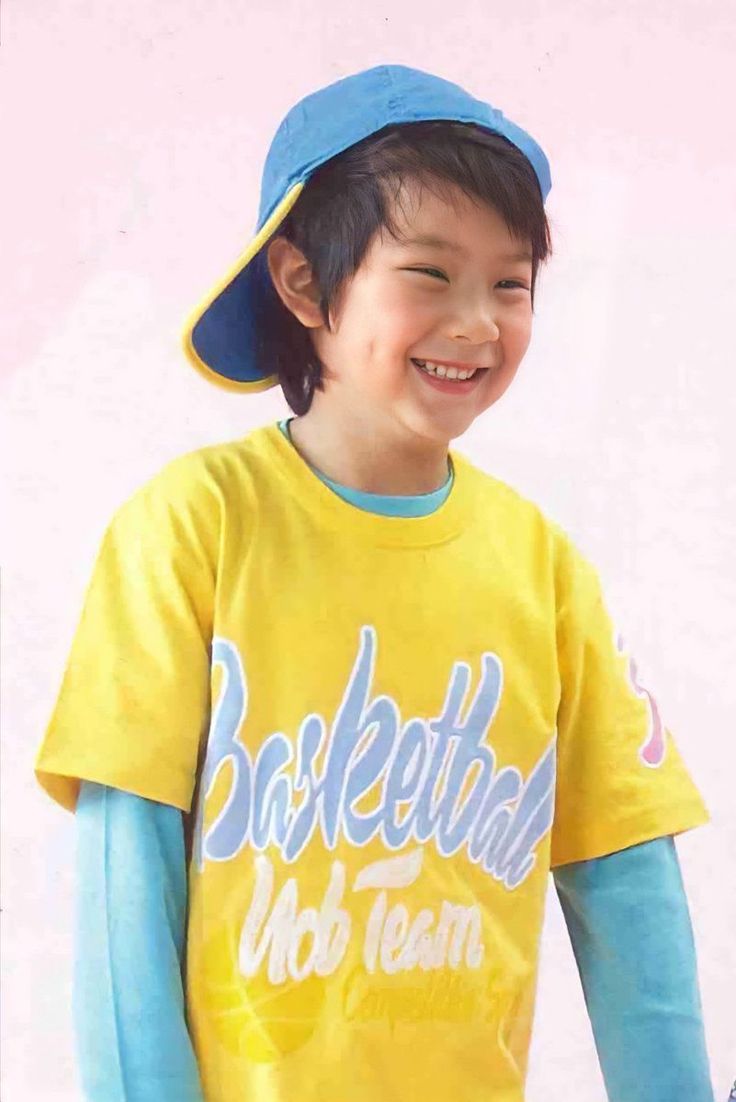 a young boy in a yellow shirt and blue hat smiles at the camera with his hands on his hips