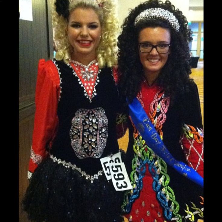 two women dressed in costumes posing for the camera with one holding a ribbon and smiling