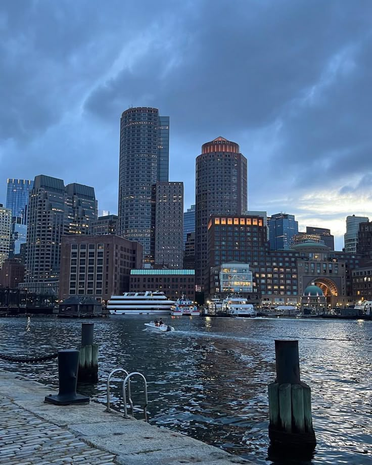 the city skyline is lit up at night with boats on the water in front of it