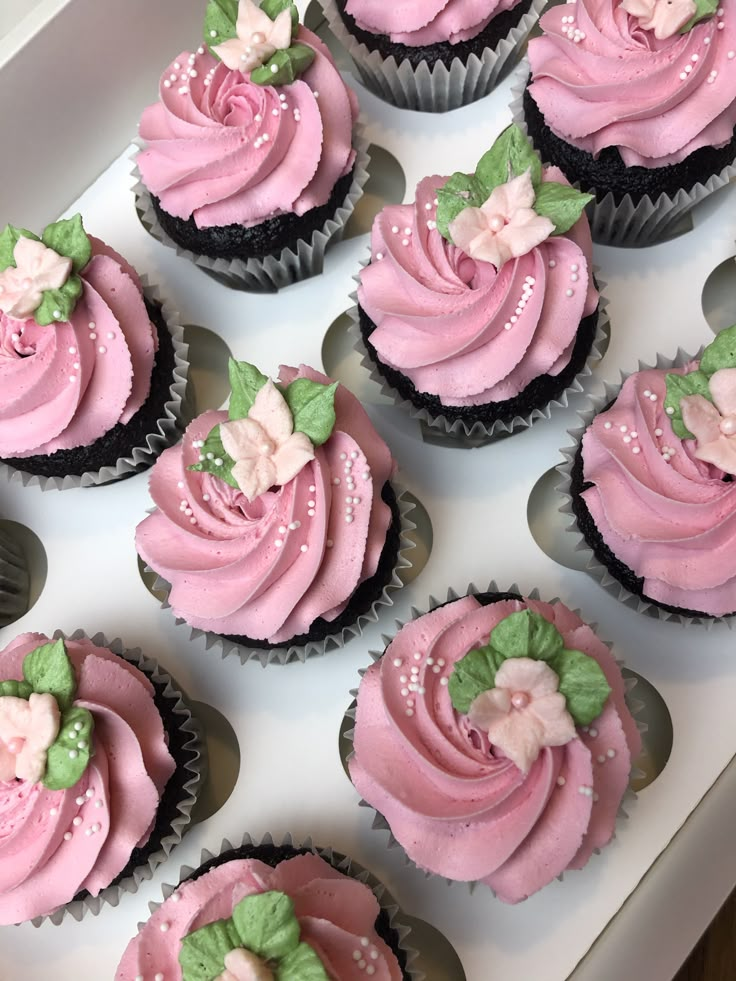 cupcakes with pink frosting and green leaves on them in a white box