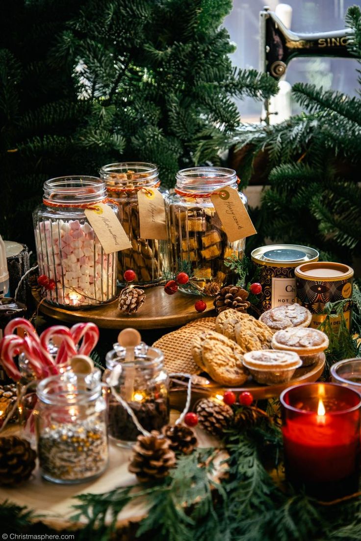 christmas cookies and candy in glass jars on a table with pine cones, fir trees and candles