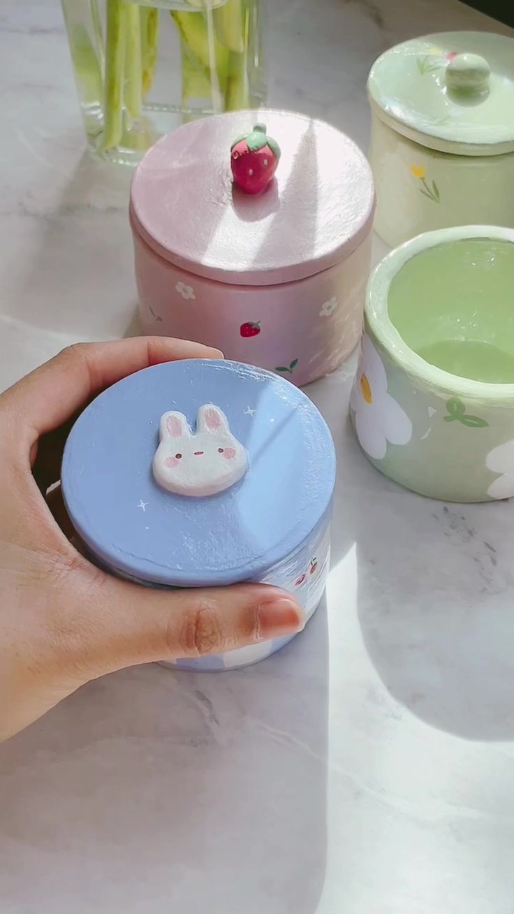 a hand holding a small plastic container with a bunny face on it and other containers in the background