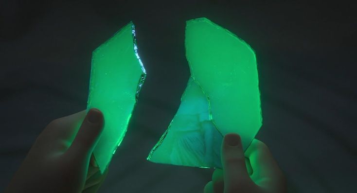 two pieces of green glass being held up in the dark