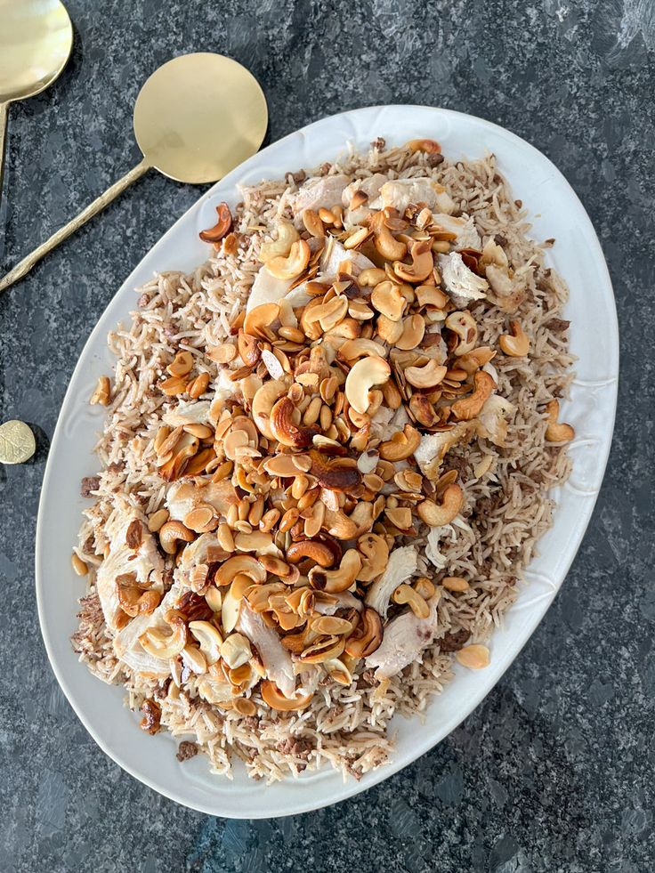 a white plate topped with rice and nuts on top of a table next to spoons