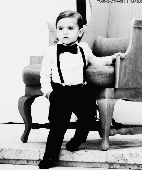 a young boy in a bow tie and suspenders sitting on the steps next to a chair