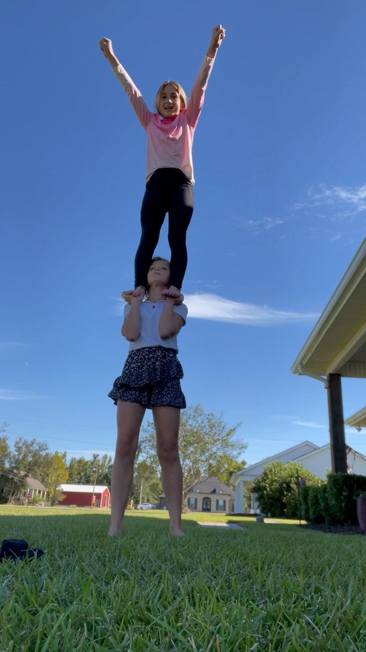 two people standing in the grass with their hands up and one person on top of them