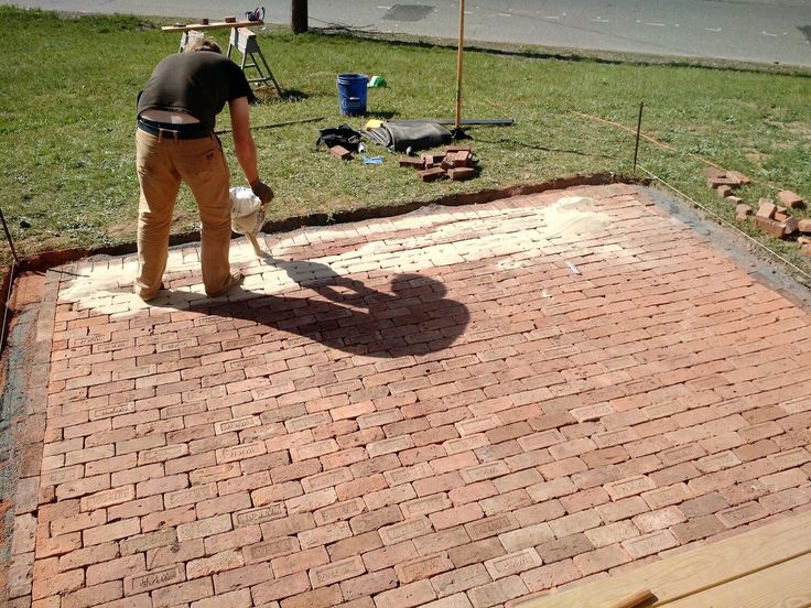 a man with a bucket and shovel is working on a brick walkway in the yard