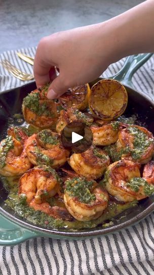 a pan filled with shrimp and vegetables on top of a striped table cloth next to a person's hand