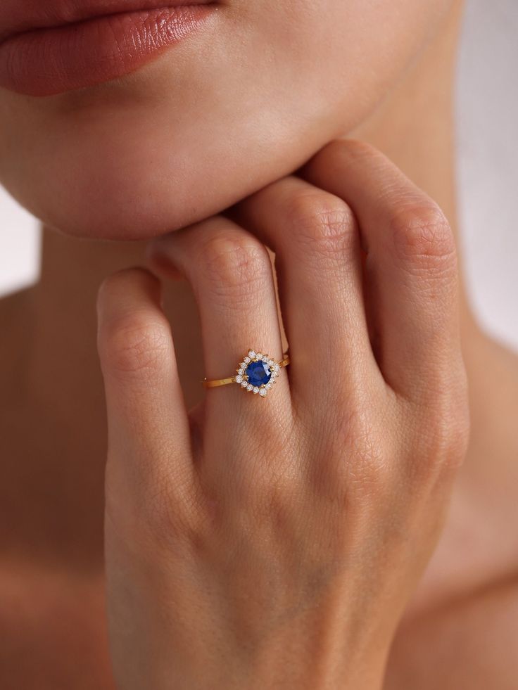 Your Blue Sapphire Engagement Ring is stylish, dainty and pretty ideal for everyday use. Details of solid gold handmade Dainty Sapphire Halo Ring are very eye-catching. It is a great gift for your loved ones. This jewelry will be an indispensable piece of yours. This meaningful Blue Gemstone Ring with high quality handwork will be a legacy you can leave to your family its.  * Sapphire and Diamond Ring Details * Material / Gold Kt:  14K (585), 18K (750), 8K (333) * Available Gold Colors: Yellow Gold, White Gold, Rose Gold * Top Width: 9.90 mm * Band Width: 1.95 mm * Band Thickness: 1.10 mm * The width may differ slightly due to handwork. * Gemstone: AAA Grade Sapphire and Cz Diamond * ABOUT PRODUCT Products with stones will be ready for dispatch within 3-5 business days, products without st Blue Birthstone Diamond Ring In 14k Gold, Blue 14k Gold Diamond Birthstone Ring, Blue 14k Gold Diamond Ring With Birthstone, Blue 14k Gold Promise Ring With Birthstone, Dainty Blue 14k Gold Rings, Sapphire Round Cut Jewelry For Proposal, Blue Birthstone Cluster Ring In 14k Gold, Blue 14k Gold Cluster Ring With Birthstone, Blue Open Ring Crystal Birthstone