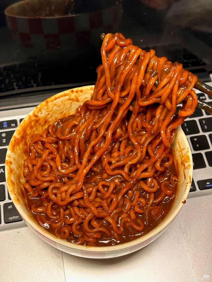 a bowl filled with noodles sitting on top of a laptop computer