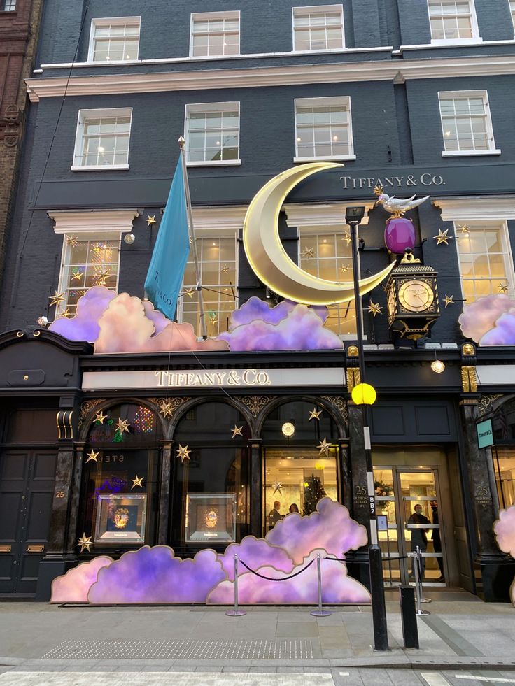 the front of a building with a clock and clouds painted on it's side