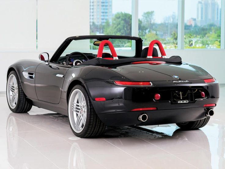 a black sports car is parked in a room with large windows and white tile flooring