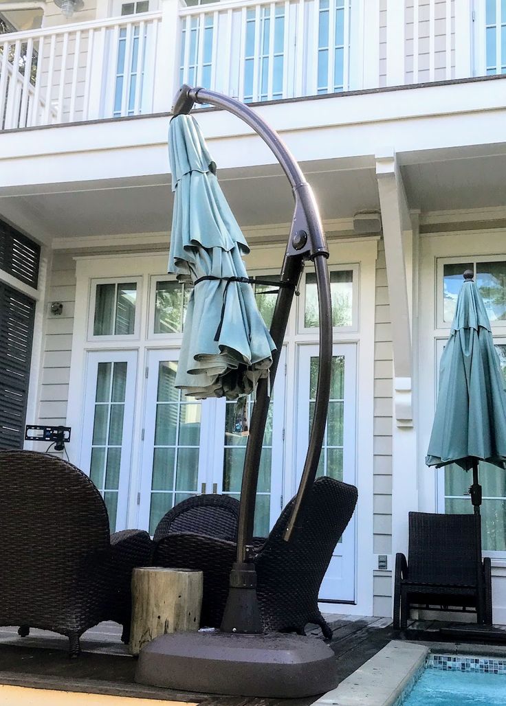 an outdoor patio with chairs and umbrellas next to a swimming pool in front of a house