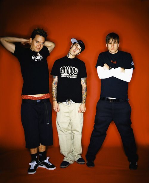 three young men standing next to each other in front of an orange wall with their arms crossed