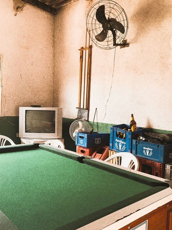 an old room with a pool table, television and fan on the wall next to it