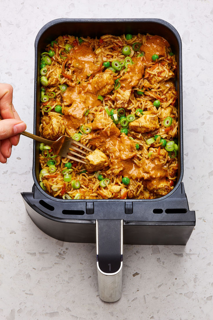 a person holding a fork in a casserole dish with meat and peas on it