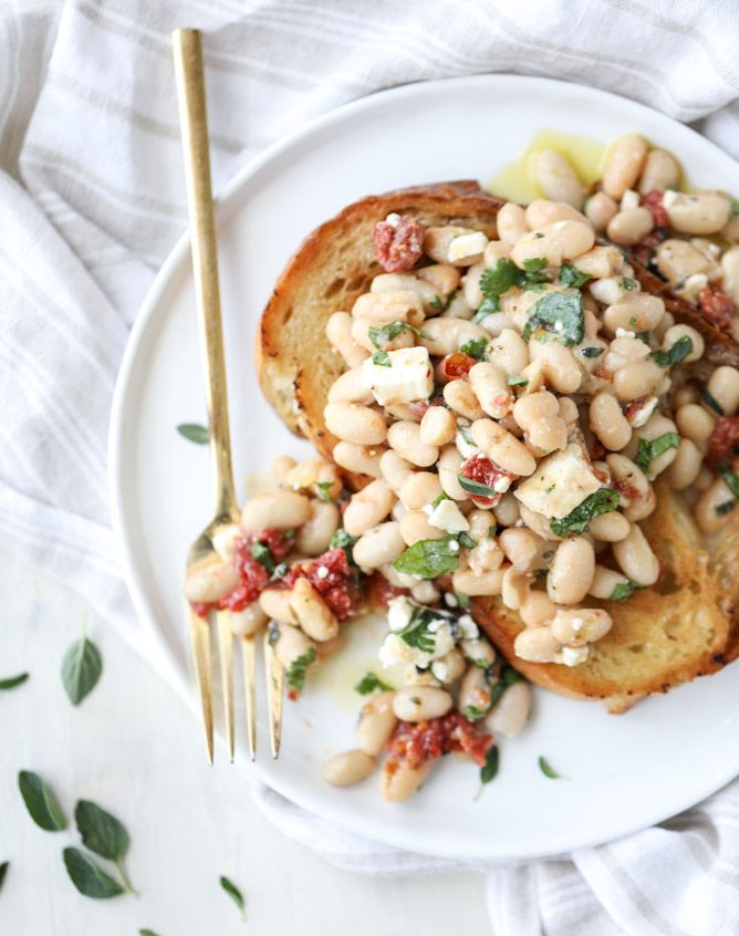 a white plate topped with beans and bread next to a fork on a table cloth