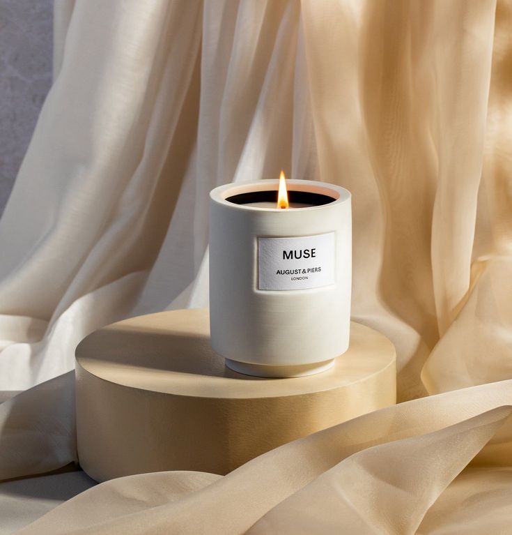 a white candle sitting on top of a wooden stand next to a beige cloth covered wall