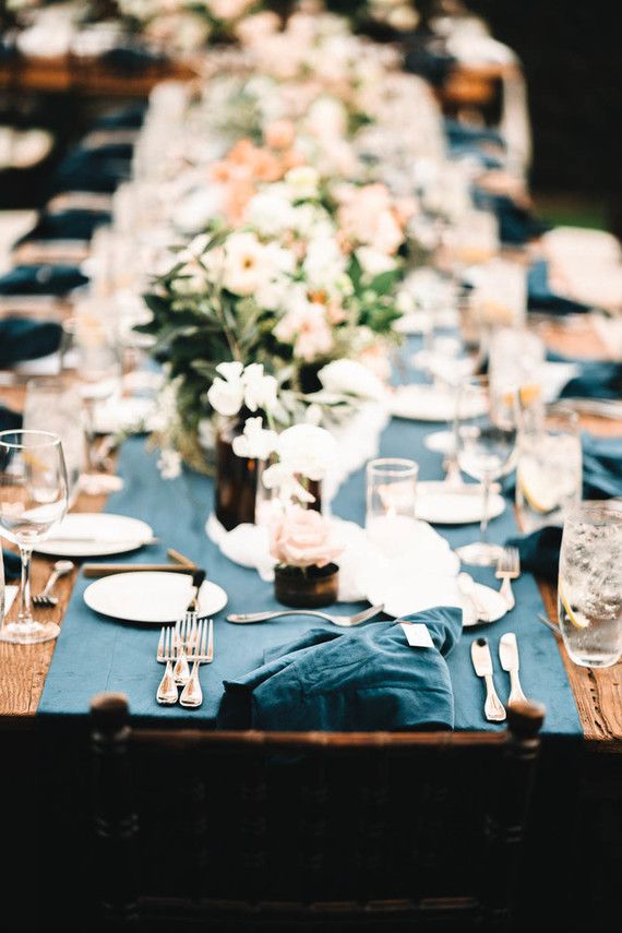 a long table is set with blue linens and place settings for an elegant dinner