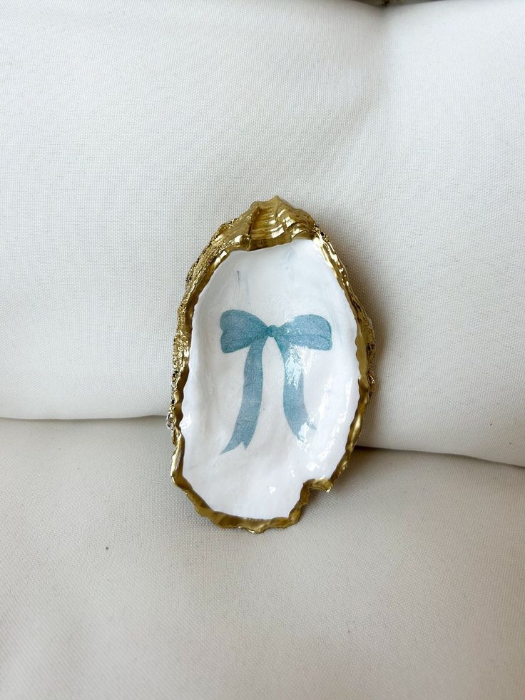 a white and gold plate with blue bows on it's side sitting on a pillow