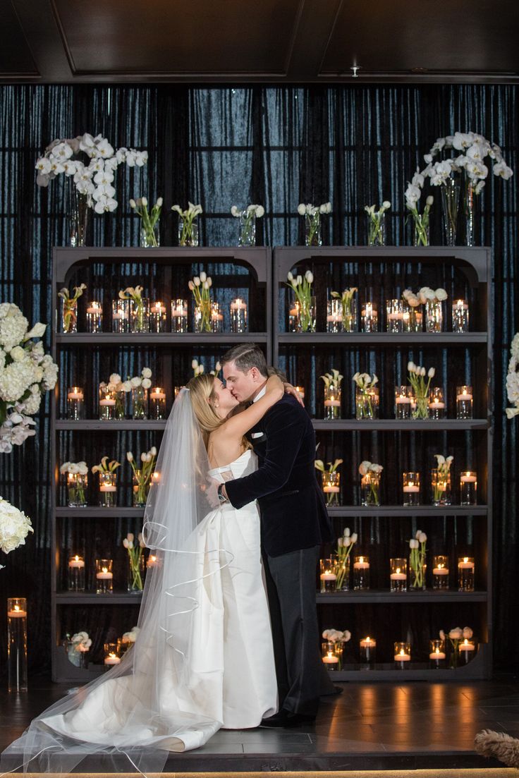 a bride and groom kissing in front of a wall of candles at their wedding reception