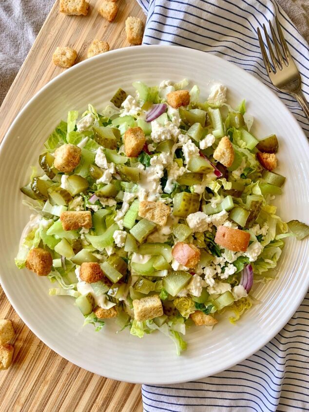 a white bowl filled with salad and croutons on top of a wooden table