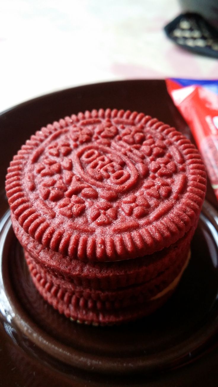 two red cookies sitting on top of a black plate next to a bag of chips