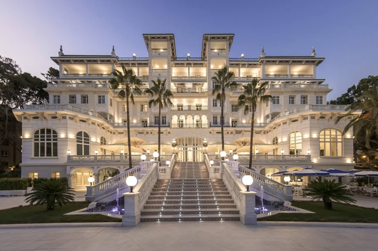 a large white building with palm trees and stairs leading up to the front entrance at night