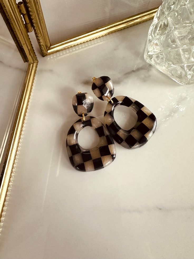 a pair of black and white checkered earrings sitting on top of a marble counter