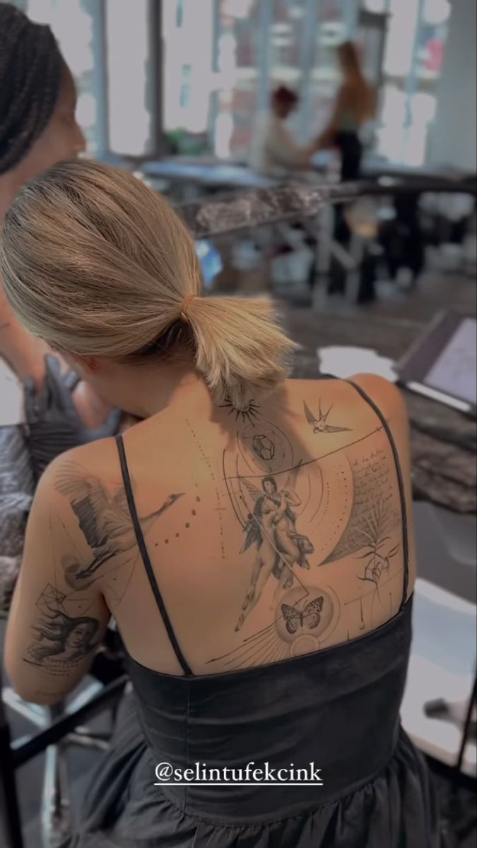 a woman with tattoos on her back sitting at a table