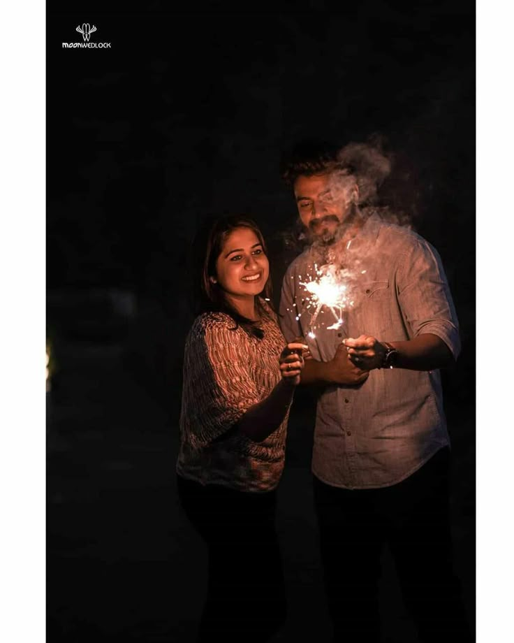 a man and woman standing next to each other holding sparklers